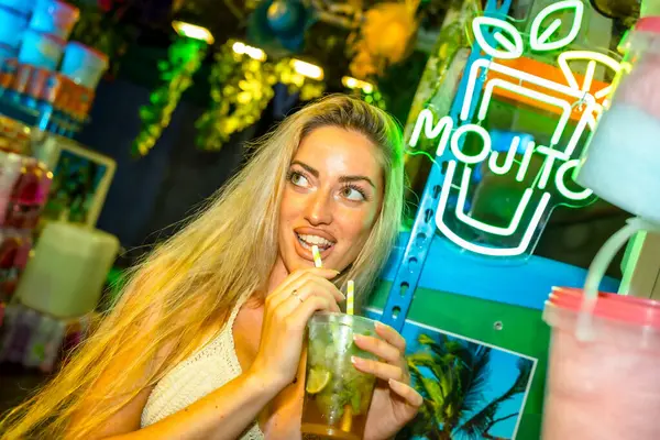 stock image Flirting blonde woman drinking a mojito cocktail in a bar at night