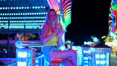 Sarışın bir kadının sağlıksız bir sosisliyi gece fuarında tutarken çekilmiş bir fotoğrafı.