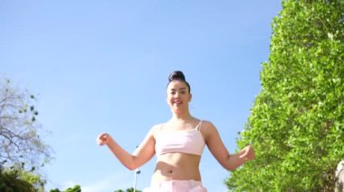 Pembe pantolonlu bir kadın kaldırımda dans ediyor. Manzara enerjik ve eğlenceli.