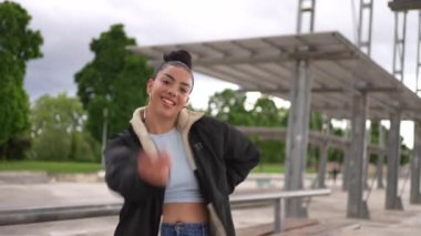 Binanın önünde bir kadın poz veriyor. Mavi bir atlet ve kot pantolon giyiyor.