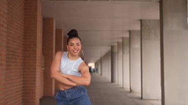 Mavi kotlu ve kolsuz tişörtlü bir kadın beton zeminde dans ediyor. Özgürlük ve neşe kavramı, çünkü kadın tamamen dansla meşgul.