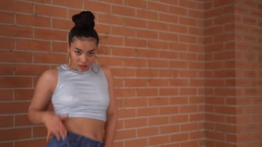 Mavi kotlu ve kolsuz tişörtlü bir kadın beton zeminde dans ediyor. Özgürlük ve neşe kavramı, çünkü kadın tamamen dansla meşgul.