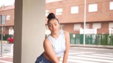 Mavi kolsuz bluzlu ve kot pantolonlu bir kadın binanın önünde dans ediyor. Sahne neşeli ve eğlenceli, çünkü kadın dans ederken eğleniyor.