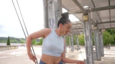 Bir kadın, kolları çaprazlanmış ve yüzünde bir gülümsemeyle bir resim için poz veriyor. Mavi bir atlet ve kot pantolon giyiyor.