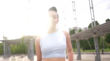 Bir kadın beton zeminde dans ediyor. O, kot pantolon ve mavi bir gömlek giyiyor. Manzara enerjik ve eğlenceli.