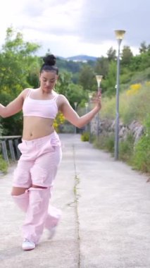 Pembe pantolonlu ve pembe bluzlu bir kadın kaldırımda dans ediyor. Özgürlük ve neşe kavramı, çünkü kadın tamamen dansla meşgul. Pembe renk şeması neşe katıyor