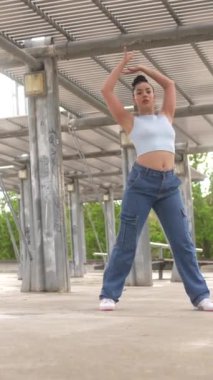 Kot pantolonlu bir kadın beton zeminde dans ediyor. Gülümsüyor ve eğleniyor.