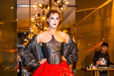 Siyah ceketli ve kırmızı etekli bir kadın fotoğraf için poz veriyor. Sahne gizemli ve ilgi çekicidir, çünkü kadının kıyafeti ve makyajı ona dünya dışı bir görünüm verir. Şehirdeki Cadılar Bayramı partisinde.