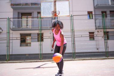 Şehirde güneşin altında basketbol oynayan Afrikalı genç bir kadının düşük açılı fotoğrafı.