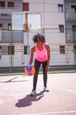 Şehir mahkemesinde tek başına basketbol oynayan esmer bir kadının dikey fotoğrafı.