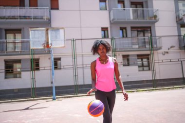 Açık hava sahasında basketbol oynayan Afrikalı Amerikalı bir kızın fotokopi çekilen yatay fotoğrafı.