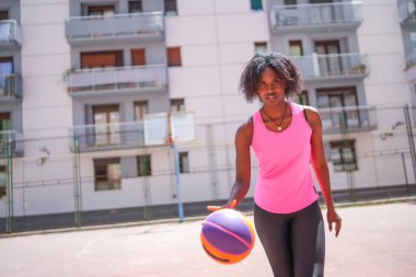Şehir basketbol sahasında salya akıtırken kameraya bakan kendinden emin bir afro kadın.
