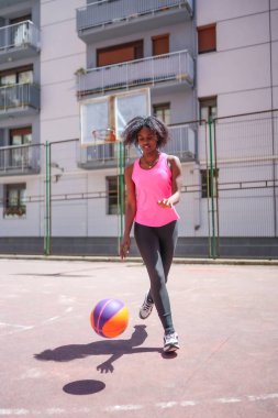 Şehir mahkemesinde basketbol oynayan Afrikalı bir kadının dikey fotoğrafı.