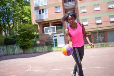 Spor kıyafetleri içinde Afro-Amerikalı bir kadın açık şehir mahkemesinde basketbol antrenmanı yapıyor.