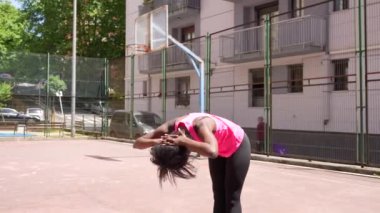 Genç bir Afrikalı Amerikalı kadının şehir basketbol sahasında esneme hareketlerini gösteren uzun bir video.