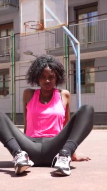 Basketbol sahasında gerinen Afrikalı genç bir kadının tam boy fotoğrafı.