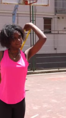 Açık hava basketbol tesisinde ısınan Afrikalı genç bir kadının dikey videosu.