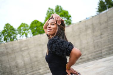 Parkta tek başına salsa yaparken gülümseyen seksi esmer kadın.