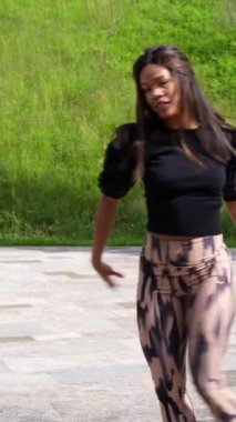 Tek başına parkta Küba salsası yapan mutlu bir Latin kadın dansçının dikey videosu.