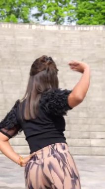 Tutkulu bir Latin kadının parkta tek başına salsa yapmasını gösteren dikey profil videosu.
