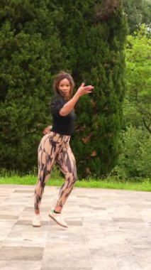 Latin bir genç dansçının parkta dans eden bir koreografiyi sahnelediği dikey bir video.