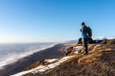 Soğuk kış mevsiminde İzlanda 'da kar yağarken Dyrholaey plajı perspektifinde bir turist.