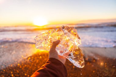 Güneş doğarken elinde bir parça buzla İzlanda 'da Jokulsarlon' un yanındaki Diamond Sahili 'nde bir adam.