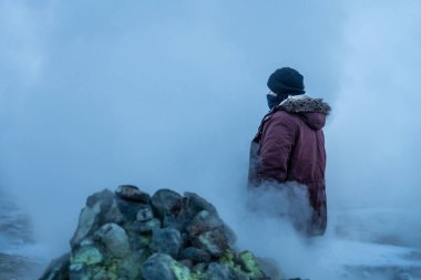 Hver veya Namafjall jeotermal parkında kışın, İzlanda 'da dumanı tüten fümerollerin arkasında yürüyen bir adam.