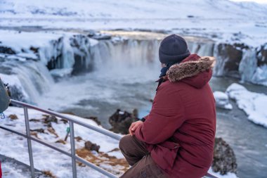 Kışın gün batımında donmuş Godafoss şelalesinde yürüyen bir adam İzlanda 'da