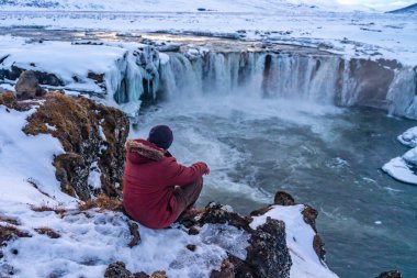 Kışın gün batımında donmuş Godafoss şelalesinde yürüyen bir adam İzlanda 'da