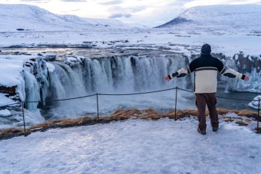 Kışın İzlanda 'da donmuş Godafoss şelalesinde kollarını açmış bir yürüyüşçü.