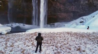 Seljalandsfoss Şelalesi 'nde kışın sırtı dönük bir fotoğrafçı, İzlanda' da karla çevrilmiş.