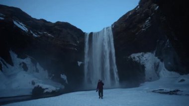 Donmuş Skogafoss şelalesinde kışın İzlanda 'da karla dolu bir turist, ıslak lens.