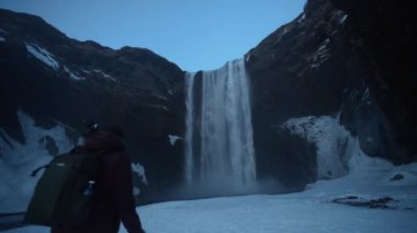 Donmuş Skogafoss şelalesinde kışın İzlanda 'da karla dolu bir turist, ıslak lens.
