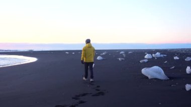 Sarı ceketli bir adam kışın Diamond Beach İzlanda 'da yürüyor.