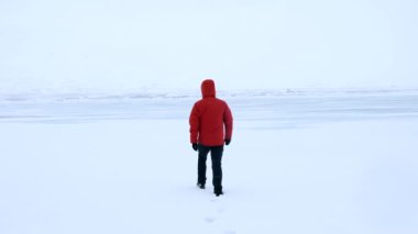 Soğuk İzlanda kışında donmuş bir gölde yürüyen genç bir adam. Kırmızı bir ceket giyiyor.