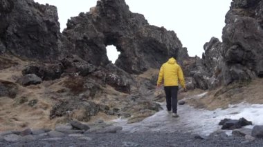 İzlanda 'nın Snaefellsnes yarımadasındaki Djupalonssandur plajında sırt çantalı bir yürüyüşçü. Sarı bir rüzgarlık giyiyordu.