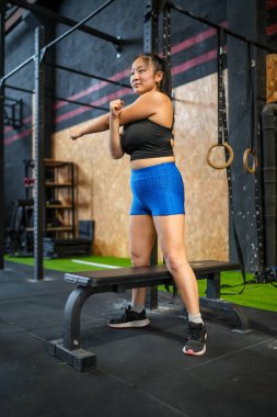 Spor salonunda egzersiz yapmadan önce esneme hareketleri yapan Asyalı güzel bir kadının dikey fotoğrafı.