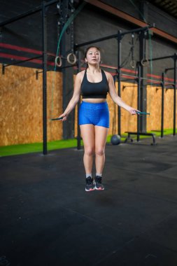 Asyalı bir sporcunun dikey boy ve ön portresi çapraz antrenman salonunda ip atlıyor.