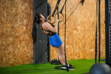 Barfiks çekmek için spor yüzükleri kullanan Asyalı bir kadının tam boy yan görüntüsü.