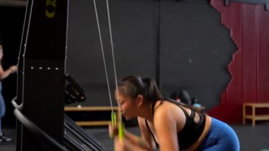 Genç ve güçlü Asyalı bir kadının spor salonunda kürek çekme makinası kullanışının uzun kenar görüntüsü.