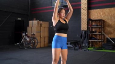 Spor salonundaki çamaşır makinesiyle ağırlık çeken Çinli bir kadının tam boy yan görüntüsü.