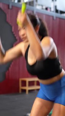 Çince güçlü bir kadının ağırlık kaldırırken çapraz antrenman yapan bir spor makinesiyle eğildiği dikey video.