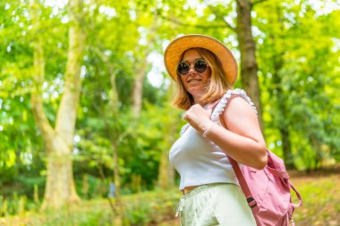 Ormanda yürürken kameraya gülümseyen güzel beyaz bir kadının yan görüntüsü.