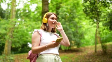 Kafkasyalı genç bir kadın gülerek ormanın içinde bir patikada dikilirken yukarı bakıyor.