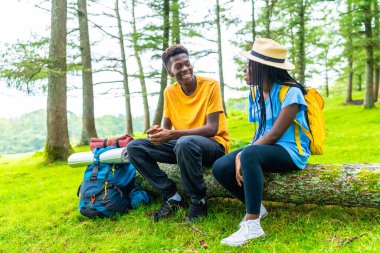 Gülümseyen genç Afrikalı çift ormanda kütüğün üzerinde oturuyor, rahatlıyor ve konuşuyorlar.