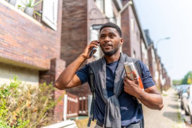 Afrikalı girişimci elinde sıcak kahve termosuyla sokakta cep telefonuyla konuşuyor.