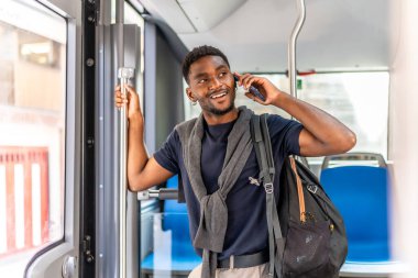 Genç Afrikalı iş adamı cep telefonuyla konuşuyor. Gülümsüyor ve otobüste duruyor.