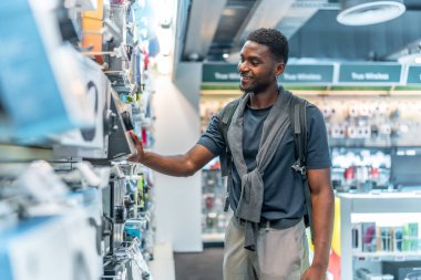 Elektronik mağazasında kulaklıkları kontrol eden Afrikalı bir adamın üç çeyrek boy fotoğrafı.