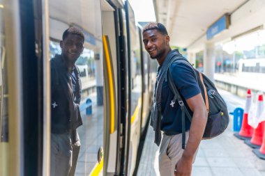Kenar manzaralı bir fotoğrafta kendine güvenen genç bir Afrikalı iş adamı şehirlerarası bir trene biniyor.